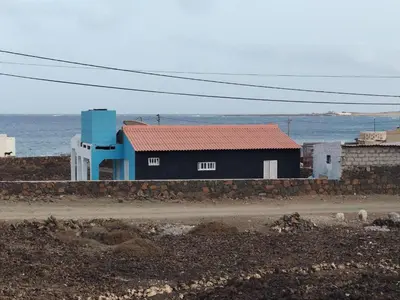a black building with a red roof next to the ocean at Villa Calhau in Mindelo