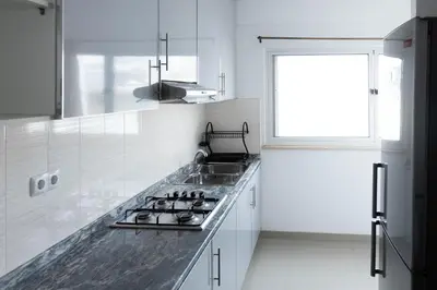 a white kitchen with a sink and a window at 2 bdr cozy apt near Praça Center, AC & Fast Wi-Fi in Praia