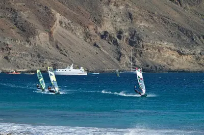 three people are windsurfing in the water with a boat at Foya Branca by Flagworld Hotels in São Pedro