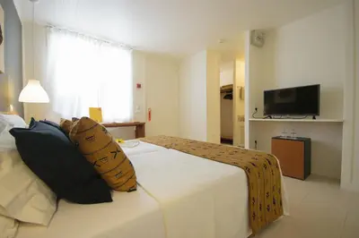a bedroom with a white bed with pillows and a television at Oasis Belorizonte in Santa Maria