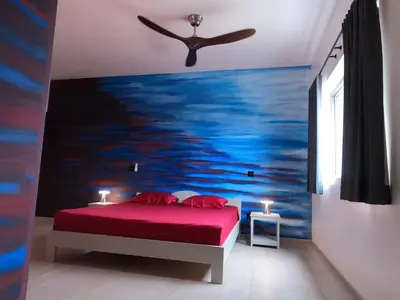 a bedroom with a red bed with a painting of the ocean at Vila Babosa in Porto Novo