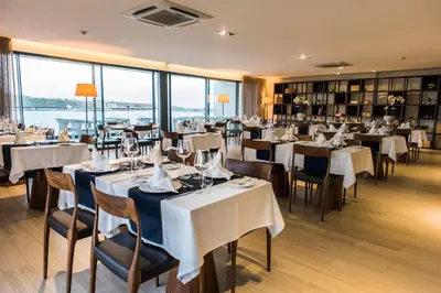 a restaurant with white tables and chairs and windows at Hotel Pérola in Praia