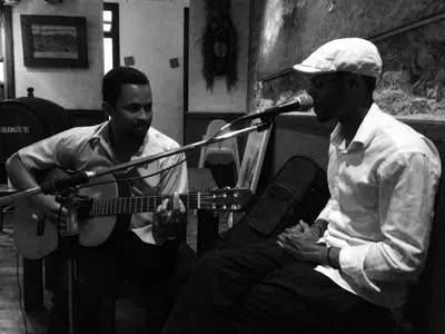 two men are singing and playing a guitar at Casa Café Mindelo in Mindelo