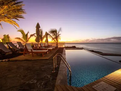 a pool with chairs and the ocean at sunset at King Fisher Village Eco-Boutique Hotel in Tarrafal