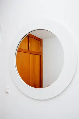 a round mirror on a white wall with a wooden door at Nhu Sao Francisco - PALMAREJO T3 in Praia