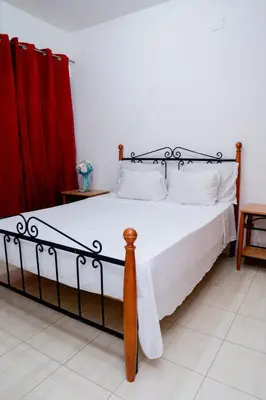 a bedroom with a bed with white sheets and red curtains at Nhu Sao Francisco - PALMAREJO T3 in Praia