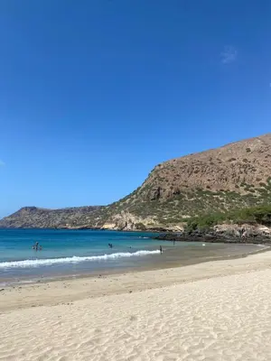 a beach with people in the water and a mountain at Casa Graciosa in Tarrafal