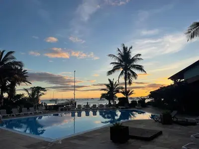 a swimming pool with palm trees and the ocean at sunset at Calma de Sal Porto Antigo II Beach apartment in Santa Maria
