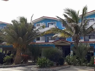 a blue building with palm trees in front of it at Apartamento Djadsal Moradias L01 próximo à praia in Santa Maria