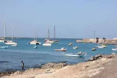a group of boats in the water with a man walking on the shore at WEYt1 in Sal Rei