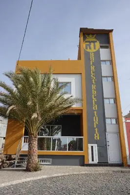 a building with a palm tree in front of it at Residencial Ribeira Torta in Porto Novo
