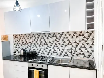 a kitchen with white cabinets and a geometric tile wall at P&SApartments in Santa Maria