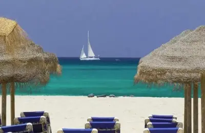 a beach with chairs and umbrellas and a sail boat in the water at Vila Verde - Chez Val in Santa Maria