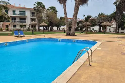 a blue swimming pool with palm trees and a building at SUNNY Apartment - SAL VILA VERDE - Cabo Verde in Santa Maria