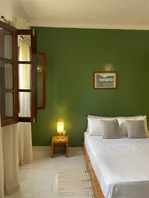 a green bedroom with a bed and a table with a lamp at Syd's Guesthouse in Praia