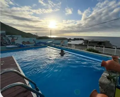 a large blue swimming pool with a view of the ocean at Fajã Beach House in Fajã