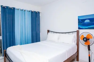 a bedroom with a bed with blue curtains and a fan at Nice And Modern with king size bed in Praia