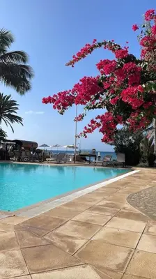 a swimming pool with blue water and pink flowers at Oceanfront Apt 25 Porto Antigo II in Santa Maria
