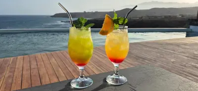 two cocktails sitting on a table next to the water at Cabo Verde Beach Sport Resort in Porto Novo