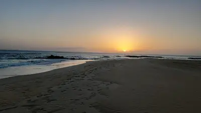 a beach with the sun setting in the ocean at Vila de Matiz in Vila do Maio