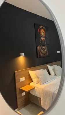 a mirror reflecting a bed with a portrait of a woman at CasaZina in Tarrafal