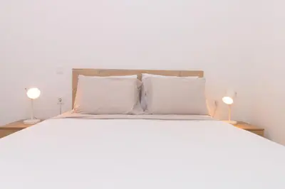 a bedroom with a bed with white sheets and two lamps at Brand New Spacious T3 Apartment in Santa Maria in Santa Maria
