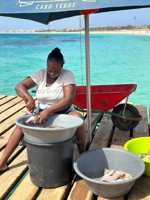 a woman sitting on a dock cooking fish in a pot at Tropical Paradise in Santa Maria