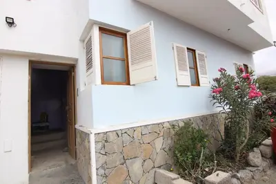 a white house with two windows and a stone wall at Kasa Tabuga in Porto Novo
