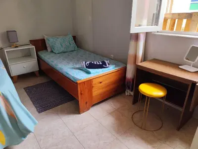 a small bedroom with a bed and a desk and a stool at Mendes Family Guesthouse, and Services in Praia