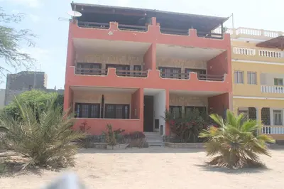 a red building with palm trees in front of it at Casa Mar Doce in Sal Rei