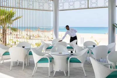 a man walking past tables and chairs at the beach at Hotel Riu Palace Boavista - All Inclusive in Boa Ventura
