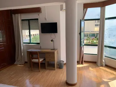 a room with a desk and a tv and two windows at Kaza Awa - Urban Guesthouse in Praia