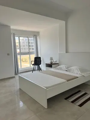 a white bedroom with a bed and a black chair at Apartamento Baia Marginal 2 in Mindelo