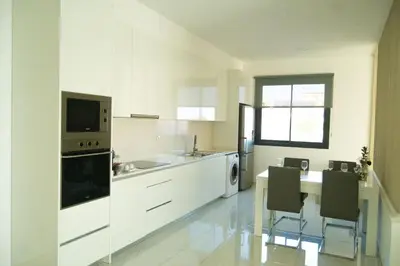 a kitchen with white cabinets and a table and chairs at Apart JC Edificio Victor in Praia