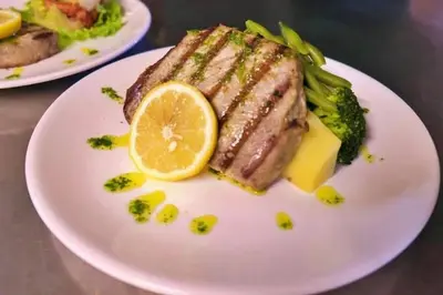 a plate with a piece of meat and broccoli with a lemon at Hotel Halcyone - Ilha do Maio in Calheta Do Maio