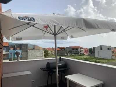 a white umbrella on a balcony with a table and a stool at Mendes Guesthouse in Tarrafal
