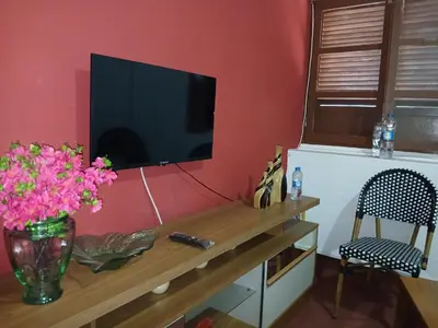 a television on a wall with a table with flowers at Mille Nuits Appartement in Tarrafal