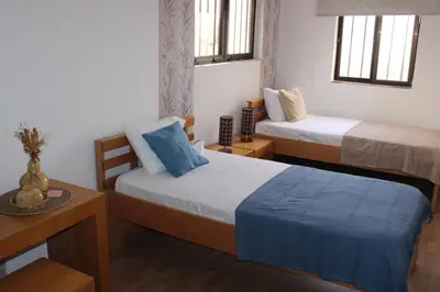 a small room with two beds and a table and two windows at brISA in Praia