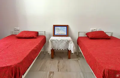 two beds with red covers in a room with a table at Casa Magui de Reis in Tarrafal