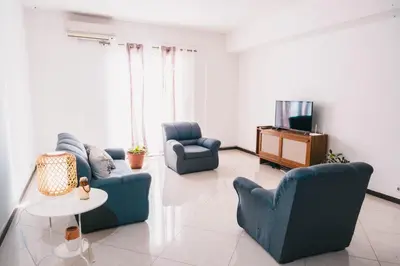 a living room with two blue chairs and a tv at T2 amplo com ar condicionado e perto da praia in Praia