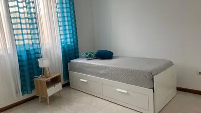 a bed sitting in a room with blue curtains at Appartement 3 chambres tout confort in Praia