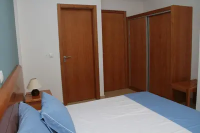a bedroom with a bed with blue pillows and wooden cabinets at Delfim Apartamentos in Praia