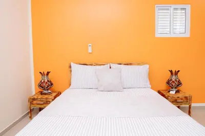a bedroom with a white bed with an orange wall at J Martins ApartHotel in Tarrafal