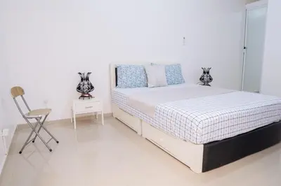 a white bedroom with a bed and a chair at J Martins ApartHotel in Tarrafal