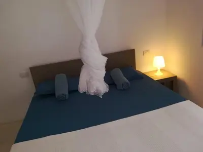 a bed with a white comforter and blue pillows at Appartamenti Praia Estoril, Sal Rei, Boa Vista in Sal Rei