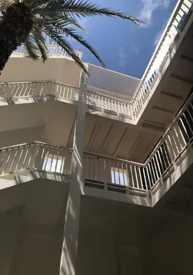 a white building with a roof and a palm tree at Appartamenti Praia Estoril, Sal Rei, Boa Vista in Sal Rei