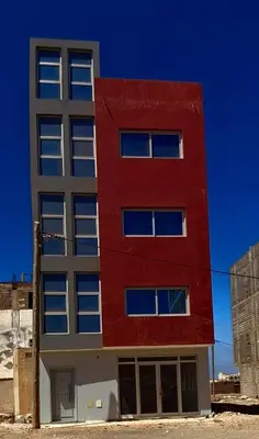 a red building with white windows on the side of it at T0 Cabral Next Door in Sal Rei