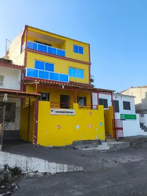 a yellow building with blue windows on a street at Catedral View Apartment in Cidade Velha