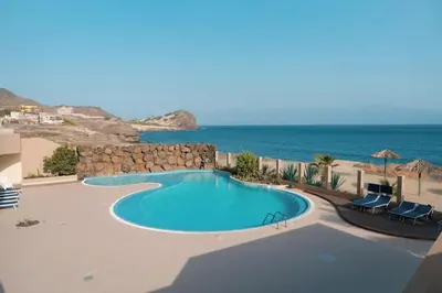 a swimming pool with chairs and the ocean in the background at Apartamento T1 - Hotel Las Rochas in Mindelo