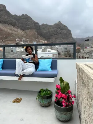 a woman sitting on a couch reading a book on a balcony at Boutique Hotel Luz da Lua in Ponta do Sol